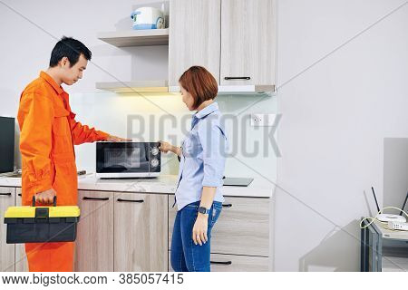Housewife Showing Broken Microwave On Kitchen Counter To Repaiman