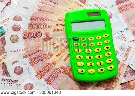 A Green Calculator Lies On A Stack Of Five Thousandth Bills Spread Out In A Fan.