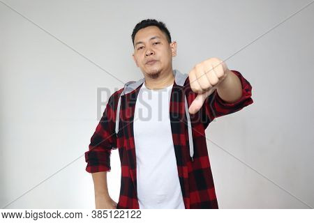 Portrait Young Asian Man Wearing Casual Shirt Shows Upset Expression With Thumbs Down, Over White Ba