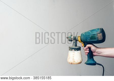 Electric Pulverizer Soiled In Paint. Green Spray Gun In Hand. White Primed Wall On The Background.