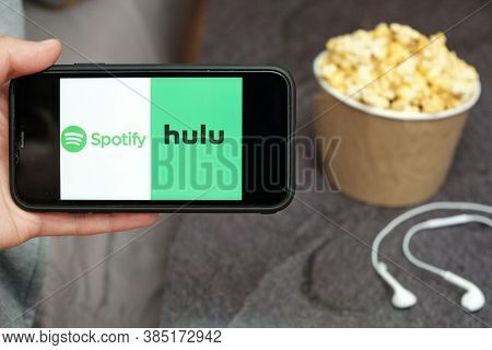 Close Up Mans Hand Holding A Mobile Phone With Spotify And Hulu Logo With Apple Earphones And Popcor