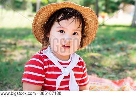 Cute Little Baby In A Red Dress And Srtaw Hat On A Picnic In The Park