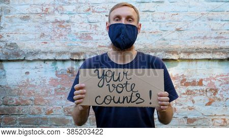 Man Shows Cardboard With Your Vote Counts Sign On Brick Wall Urban Background. Voting Concept. Polit