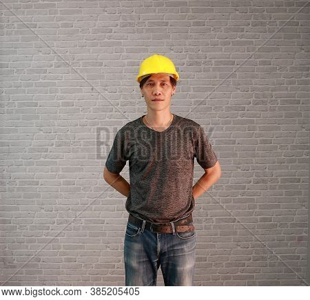 Technician Man Ware Yellow Helmet With Dark Grey T-shirt And Denim Jeans Standing And Hands Behind B