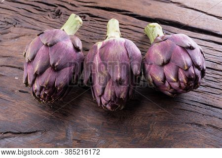 Green and purple artichoke flower edible buds on wooden background.