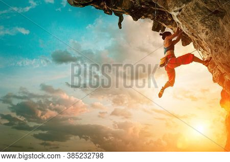 Athletic Woman Climbing On Overhanging Cliff Rock With Sunset Sky Background