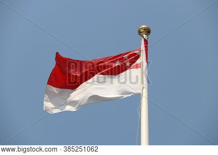 National Flag Of Singapore On Bright Blue Sky Background. Blown Away By Wind. Singapore Is One Of Th