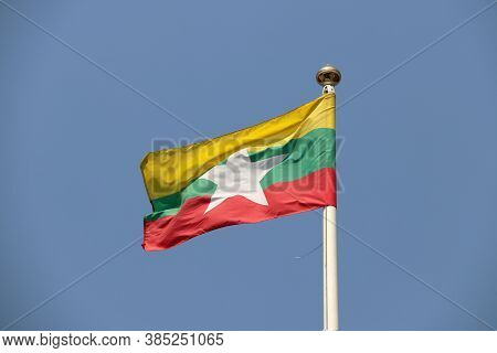 National Flag Of Myanmar On Bright Blue Sky Background. Blown Away By Wind. Myanmar Is One Of The Te