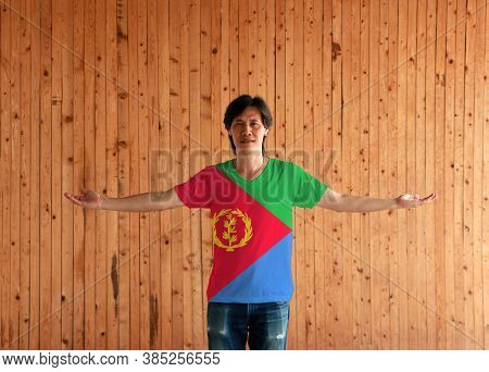 Man Wearing Eritrea Flag Color Shirt And Standing With Arms Wide Open On The Wooden Wall Background,