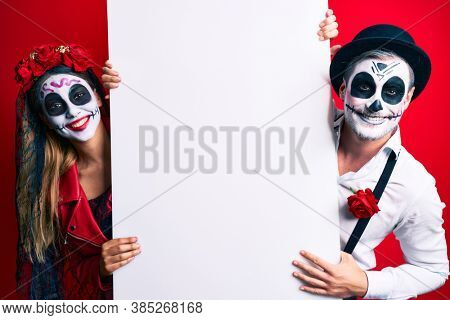 Couple wearing day of the dead costume holding blank empty banner looking positive and happy standing and smiling with a confident smile showing teeth 