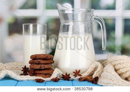 Jarra e copo de leite com biscoitos em malhas de gola alta na mesa de madeira no fundo da janela