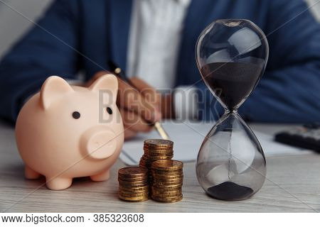 Businessman Approves Important Contract In Office. Pink Piggy Bank With Stack Of Coins And Hourglass