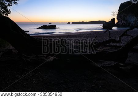 Golden Sunrise Glow On Horizon Beyond Silhouette Beach Foreground At Cathedral Cove Hahei, New Zeala
