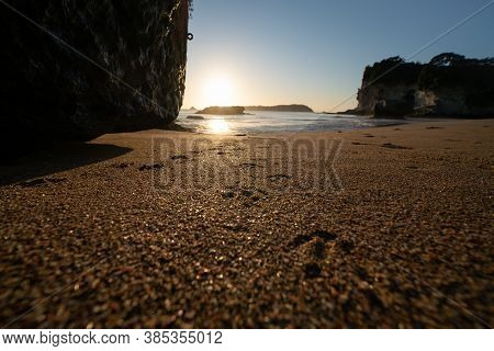 Sunrise Glow Over Grainy Sand With With Bird Footprints To Waters Edge At Cathedral Cove  On Coroman