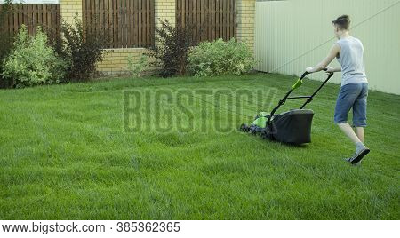 A Teenager Mows The Lawn With A Lawn Mower.