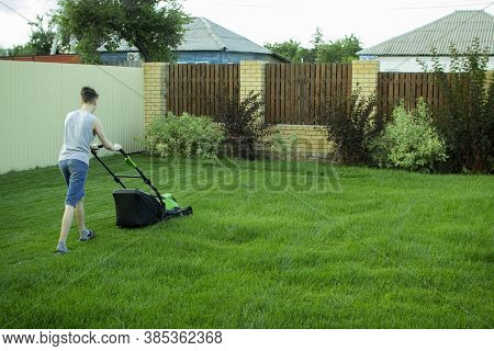 A Teenager Mows The Lawn With A Lawn Mower.