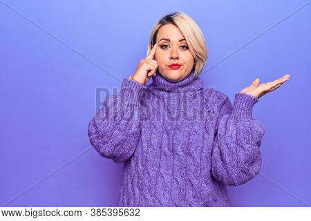 Beautiful blonde plus size woman wearing casual turtleneck sweater over purple background confused and annoyed with open palm showing copy space and pointing finger to forehead. Think about it.