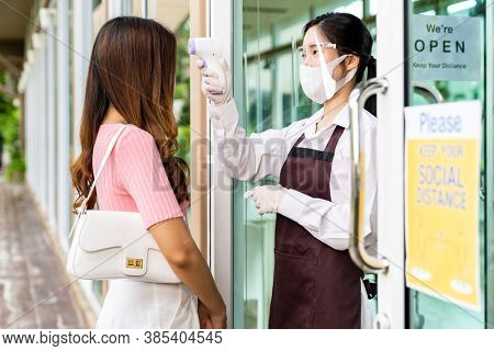 Asian waitress with face mask taking temperature to female customer woman before getting in restaurant. New normal restaurant concept after coronavirus covid-19 pandemic.