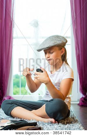 Familie - Kind oder Jugendlicher mit Mütze im Zimmer auf dem Boden sitzen und tut Make-up