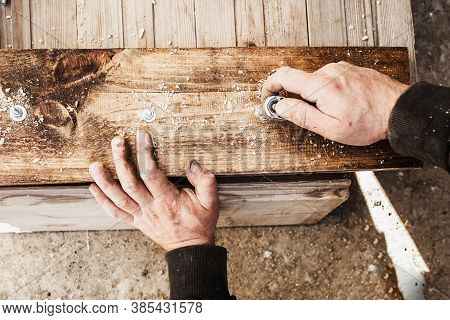 Male Hands Screw A Bolt With A Screwdriver Into A Wooden Board.