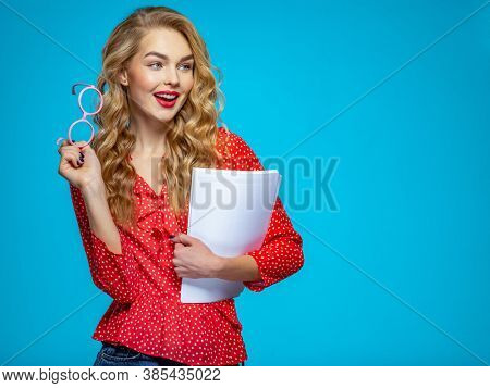 Businesswoman in a casual clothes holds papers looking away. Woman secretary in a red shirt over blue background holding documents.  Female student in a pink glasses holding documents  