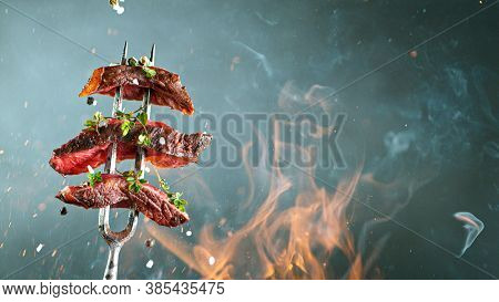 Close-up of tasty beef steak on black fork, fire flames in foreground