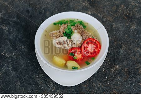 Delicious Soups Of Bone And Stew Meat With Tomatoes, Potatoes, And Sliced ​​leek In A Bowl