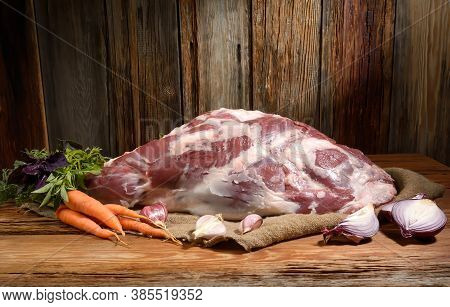 On A Wooden Table Lies A Raw Leg Of Mutton On The Bone Pierced With A Kitchen Knife . Sheep Meat Wit