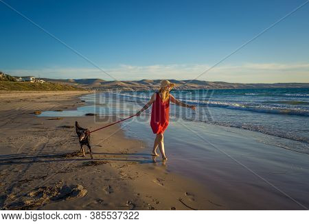 Happy Attractive Mature Woman With Her Pet Walking On Friendly Dog Beach At Sunset