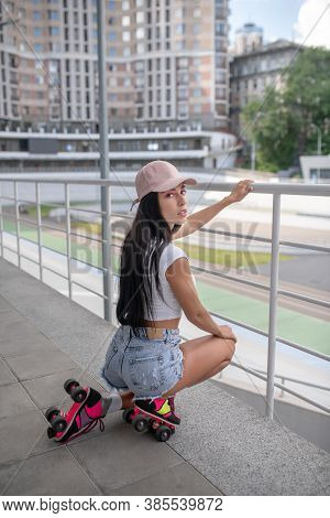 Dark-haired Girl In Jeans Shorts Sitting On Her Hunkers And Looking Thoughtful