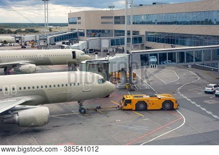 Pushback Truck Is Towing The Aircraft To A Parking Lot, A Row Of Planes Along The Terminal Building