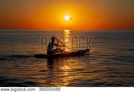 Silhouette Of A Man Floating On A Board With An Oar. Dawn Sun On The Sea. Swimming On A Supboard. Wa