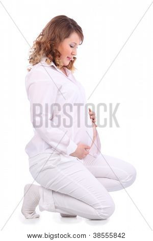 Sorridente donna incinta in bianco squat su cosce e detiene e guarda al suo ventre isolato sulla Pentecoste