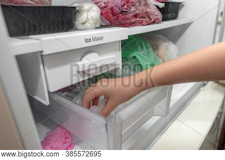The Girl Takes Ice From The Ice Maker Of The Freezer For Cooling Drinks.