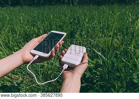 Power Bank And Smartphone In The Girl's Hand. Against The Backdrop Of Nature.