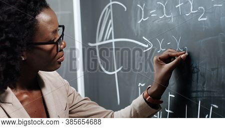 Close Up Of African American Young Woman Teacher At School Writing Formulas And Mahematics Laws On B