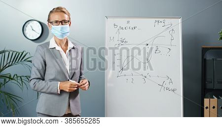 Caucasian Young Woman Teacher In Medical Mask At School Writing Formulas And Mahematics Laws On Blac