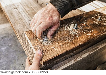 Male Hands Screw A Bolt With A Screwdriver Into A Wooden Board. Close-up, Selective Focus