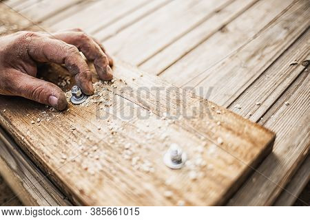 Male Hands Screw A Bolt Into A Wooden Board