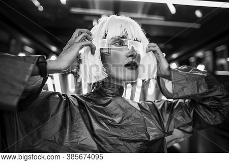 A Woman In A Futuristic Metallic Dress With Glasses Looks Ahead.