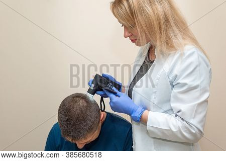 The Doctor Examines The Patient's Scalp Using An Optical Device