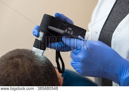 The Doctor Examines The Patient's Scalp Using An Optical Device
