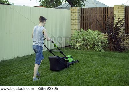 A Teenager Mows The Lawn With A Lawn Mower.