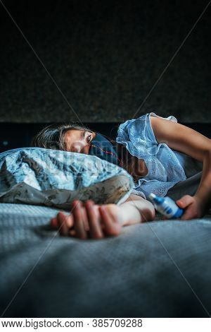 The Young Girl Is Sick. She Lies On The Bed. She Is Sad, She Has A Medical Mask On Her Face.