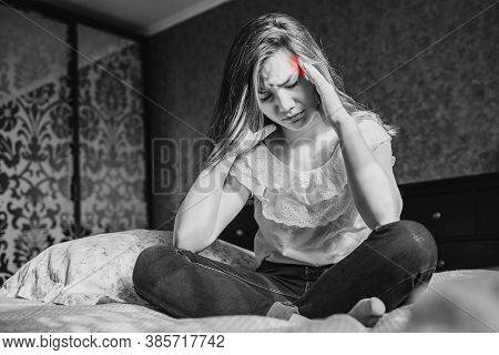 A Sad Dark-haired Girl In A White Blouse And Blue Jeans Is Sitting On The Bed In Her Bedroom. She Ha