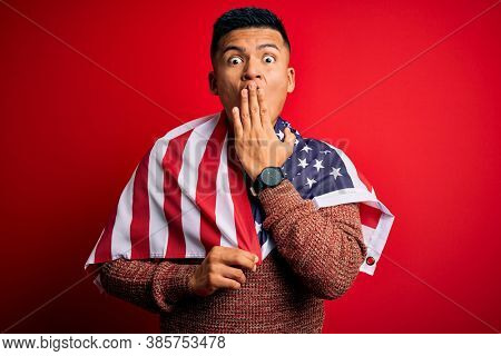 Young handsome latin patriotic man wearing united states of america falg cover mouth with hand shocked with shame for mistake, expression of fear, scared in silence, secret concept