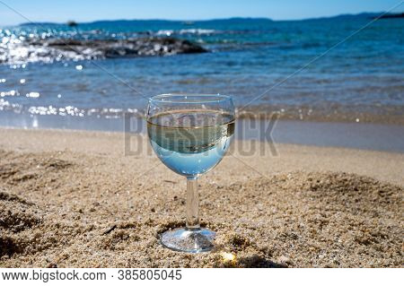 Glass Of Local Dry White Wine On White Sandy Beach And Blue Mediterranean Sea On Background, Near Le