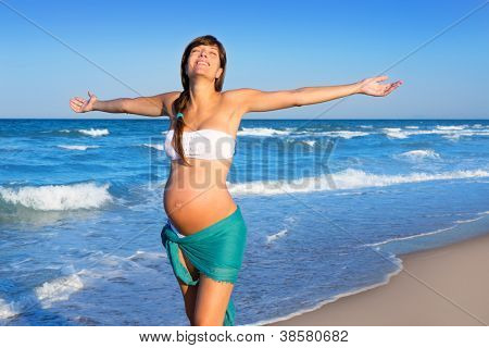Bella donna incinta camminando sulla spiaggia blu in vacanza estiva con le braccia aperte