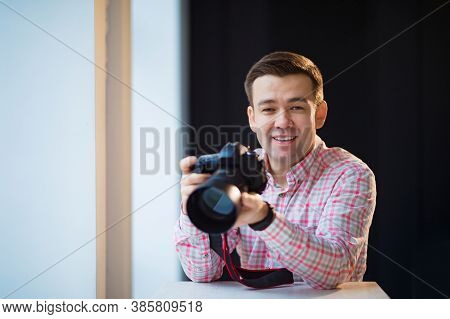A Male Photographer In A Checkered Shirt Sits At A Table And Holds A Camera In His Hands. Creative P