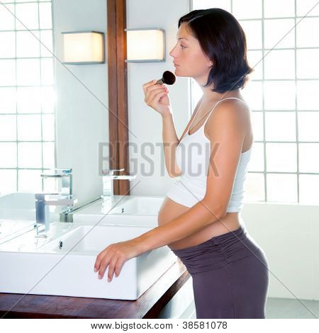 Bella donna incinta sul trucco di bagno moderno con pennello nello specchio